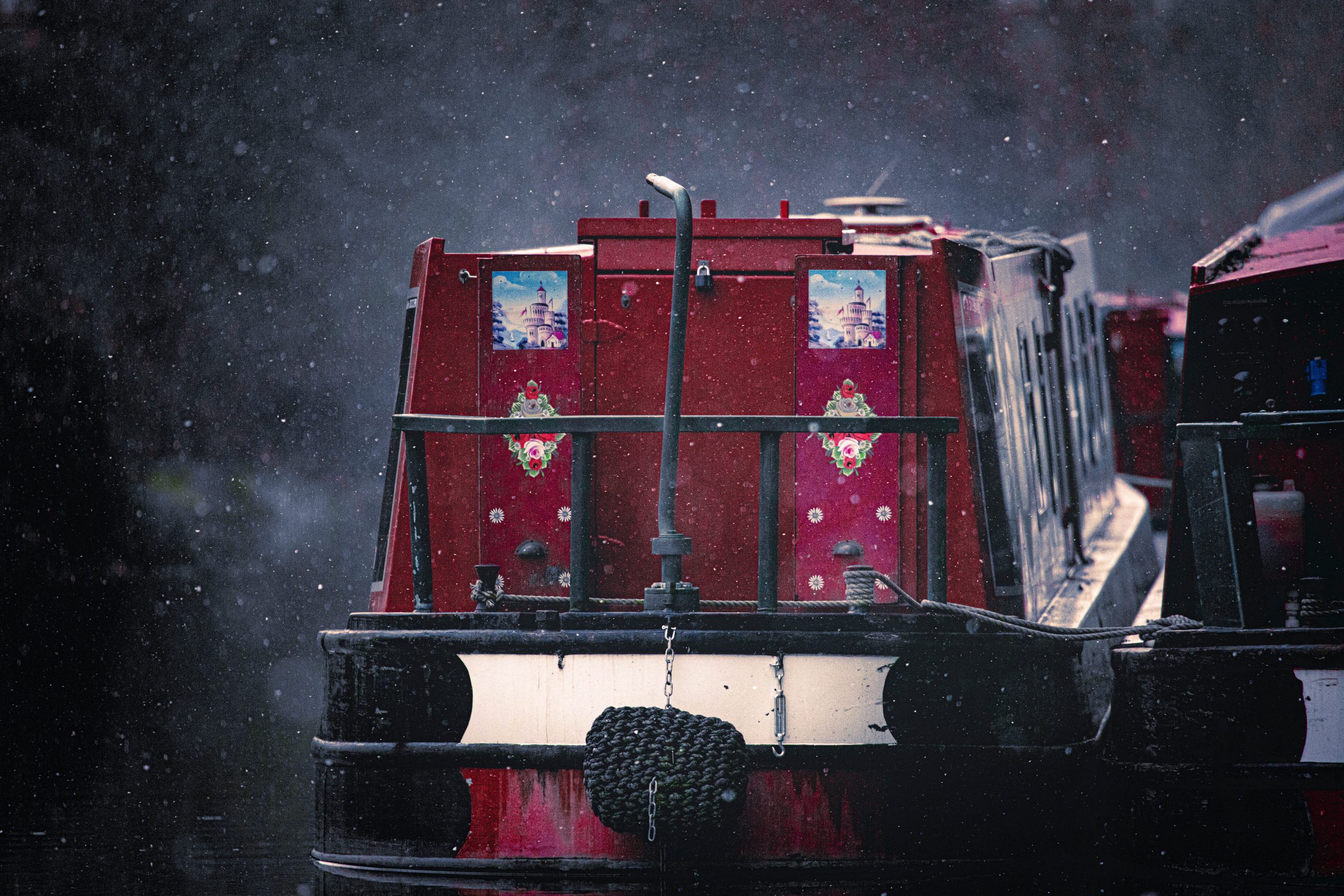 Winter Photography showing the dark maroon colour of the narrow boat moored on the Kennet and Avon Canal stands out as the Winter snow starts to fall.