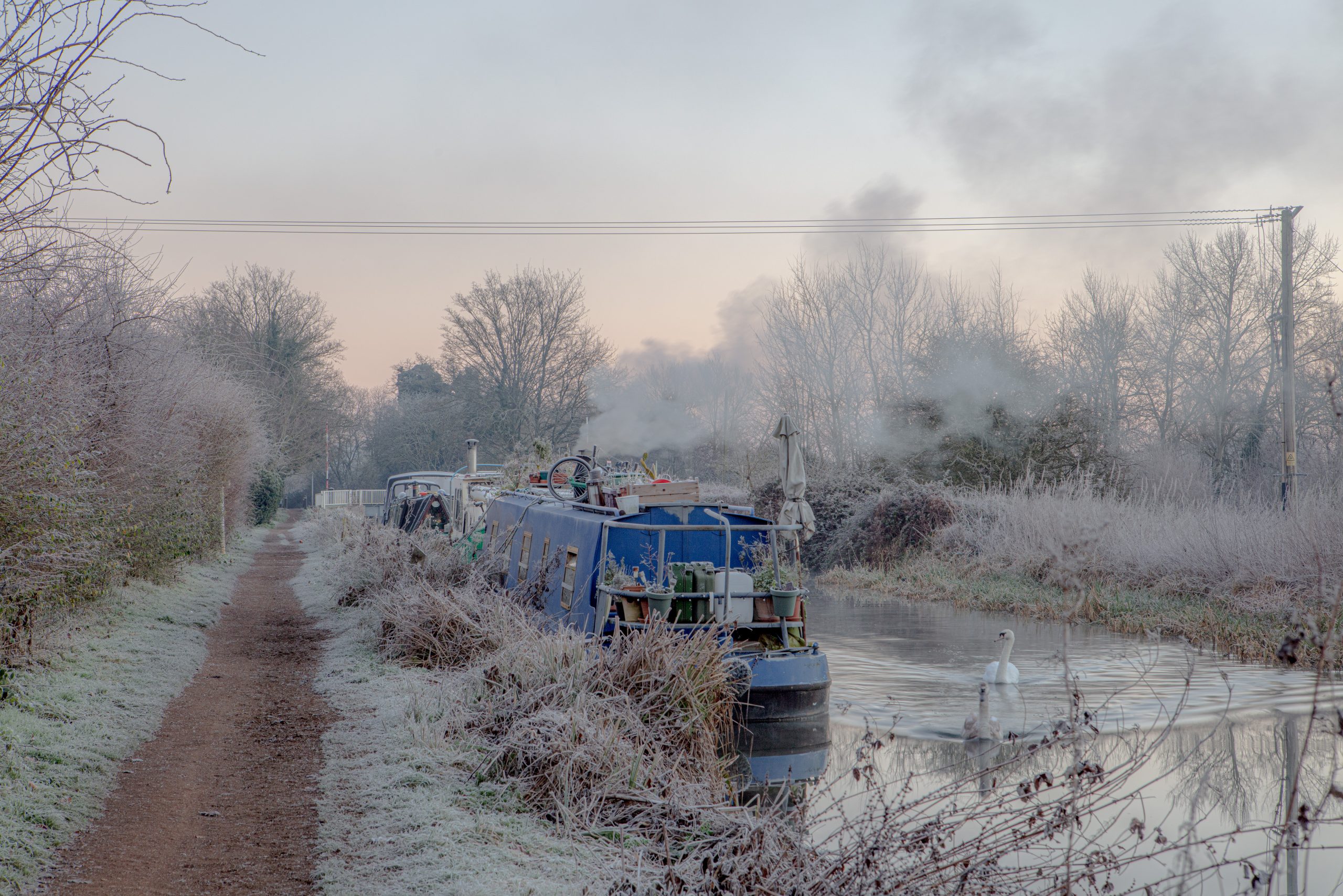 Winter morning on the Kennet and Avon Canal with narrow boats moored, smoke rising from cabin stoves, and a cold blue light at dawn.