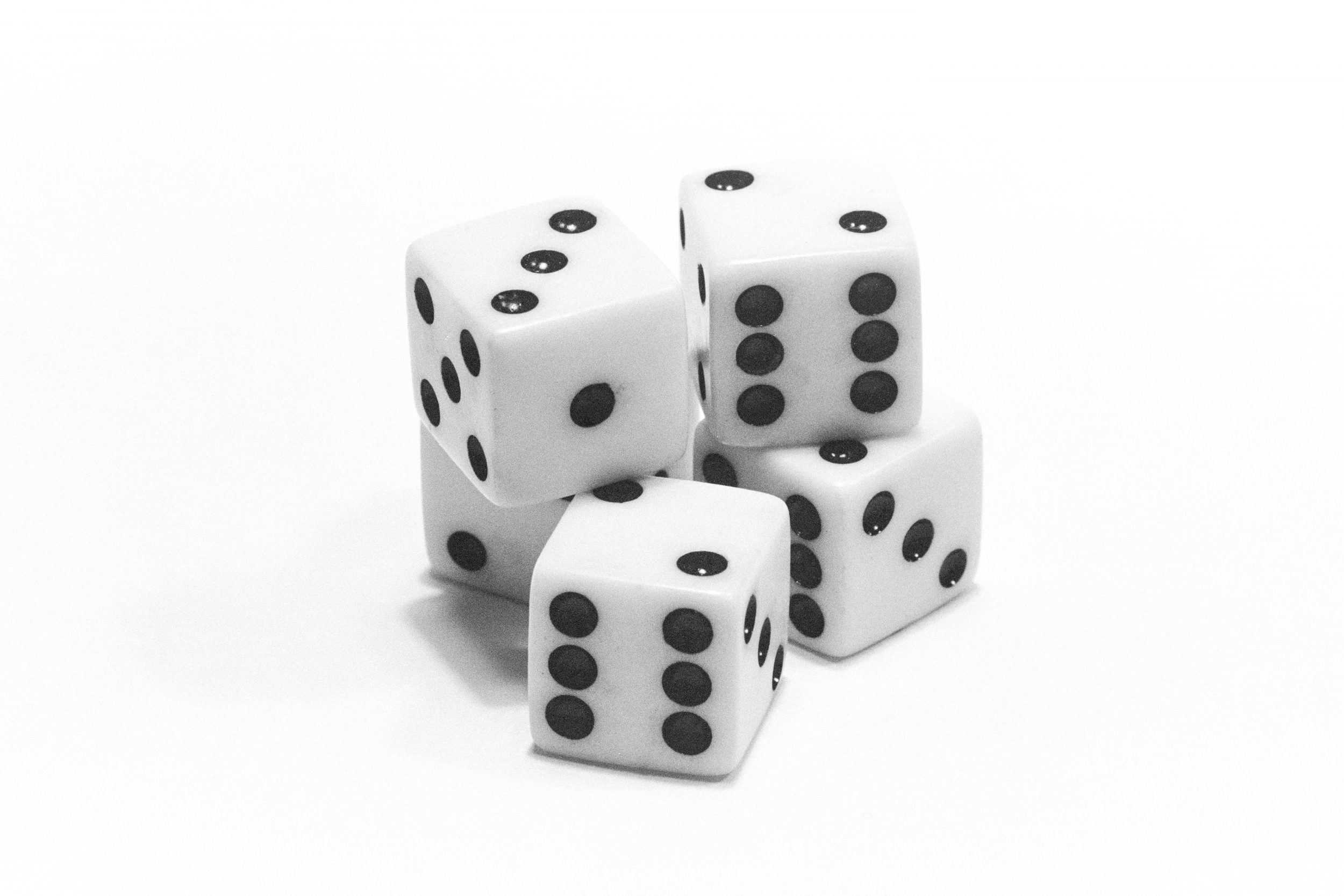 Dice - Roll of Fate - A striking black-and-white 35mm film photograph featuring a set of classic six-sided dice. The dice are scattered, their smooth edges and indented pips highlighted by dramatic, high-contrast lighting. Shadows cast by the dice create a sense of depth and intrigue, emphasising the vintage film aesthetic with its subtle grain and soft tonal gradations. The composition draws attention to the randomness of their arrangement, evoking themes of chance and unpredictability.