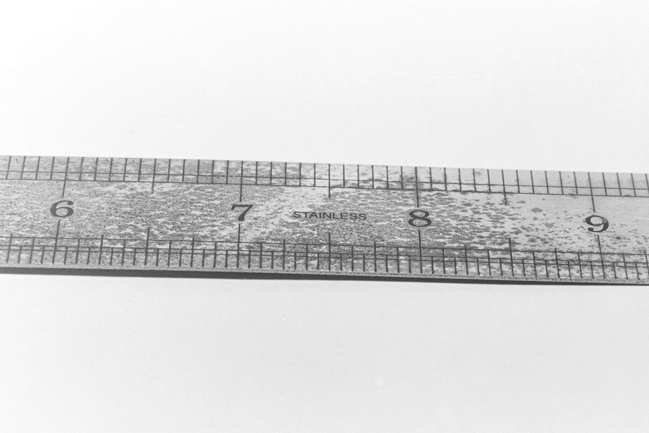 Rule Inch Markings - The close-up image captures the intricate texture and grain of an aging steel rule, showcasing the inch markings in a mesmerising black and white monochrome palette. The lines and shapes create a captivating abstract drawing, reminiscent of a meticulous sketch. The image evokes a sense of precision and craftsmanship.